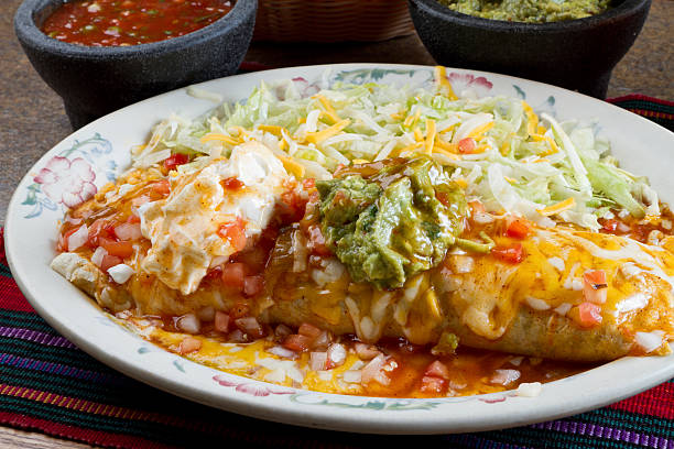 This is a mexican burrito with red sauce on top with rice and salad on the side