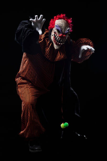 A smiling clown looks at himself in a small mirror, he wears an Andean hat and a Peruvian sports shirt, on a black background.