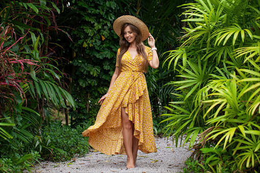 Young woman in a stylish summer dress enjoys the beauty of a tropical resort, walking among palm trees and embracing the vacation vibes. Concept of travel and summer relaxation.