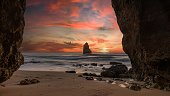 Scenic view of Camilo beach in Algarve featuring the rocky cliffs engulfed by waves at pink sunrise
