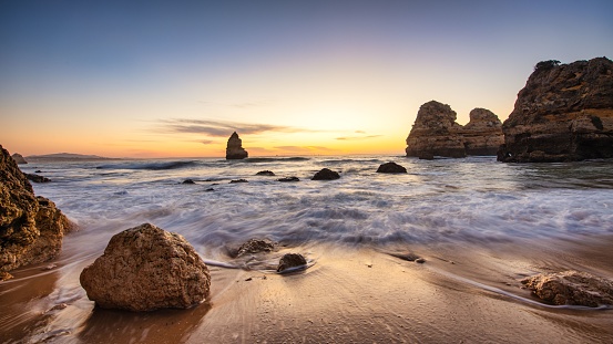 A scenic view of Camilo beach in Algarve featuring the rocky cliffs engulfed by waves at calm sunrise
