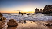 Scenic view of Camilo beach in Algarve featuring the rocky cliffs engulfed by waves at calm sunrise