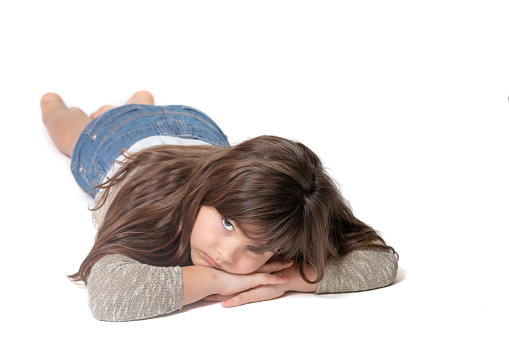 Cute sad girl is lying on the floor with her arms crossed and looking at the camera. White background .