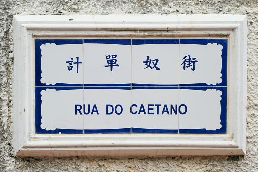 Street sign in Chinese and Portuguese made from ceramic tiles on the island of Coloane, Macau. This street is the location of the Chapel of Saint Francis Xavier, which until the late 1990s held a relic of Saint Francis Xavier and relics of Catholic martyrs killed in Japan.  This image was taken on a sunny afternoon on 5 July 2023.