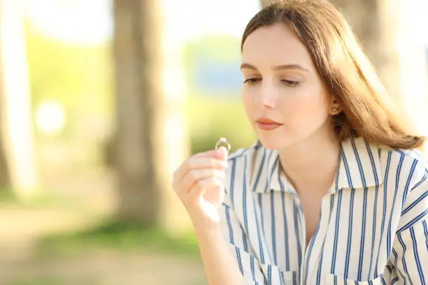 Photo of Pensive fiancee looking at engagement ring in nature