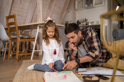 Young father and daughter drawing in a notebook while relaxing at home.