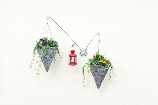 Two hanging baskets containing flowers and plants and a red lantern fixed to a wall