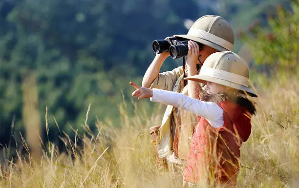 Children brother and sister playing outdoors pretending to be on safari and having fun together with binoculars and hats