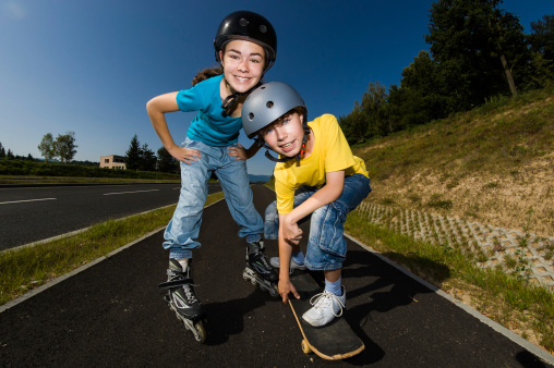 Young girl roller-blading, boy skateboarding