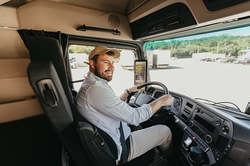 Mid adult man sitting behind the steering wheel of the semi truck and driving