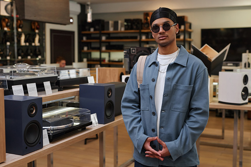 Portrait of black young man wearing stylish outfit standing in music store and looking at camera, copy space