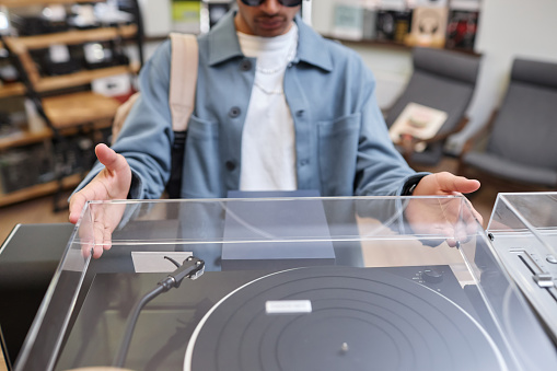 Closeup of black young man opening lid pn record player in music store, copy space