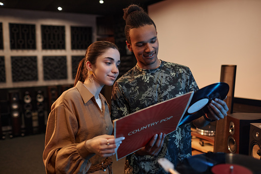 Waist up portrait of young couple holding vnyl records while enjoying music evening at home