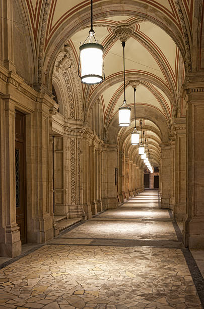 Elegant chandeliers dangle beneath vaulted ceilings adorned with columns and arches, casting warm light that lends the room a refined and majestic ambiance