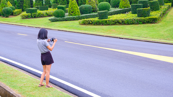Side view of Asian female tourist using digital camera to taking picture of beautiful green topiary garden on roadside in the hill