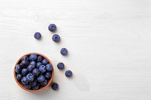 Tasty blueberry berries in a bowl on a white wooden table. place for text. top view