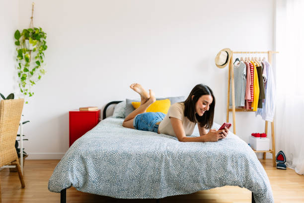 istock Happy young woman using mobile phone lying in bed at home 1550371575