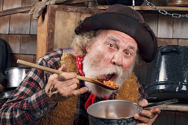 istock Hungry old cowboy eating beans from a saucepan 155037281