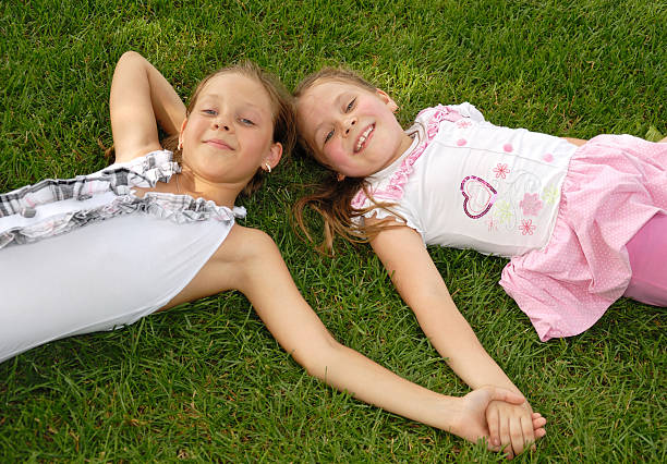 Two little girls lie on a green grass and to hold a hand