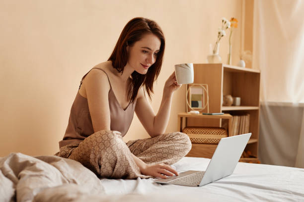 istock Young woman using laptop on bed at home end enjoying coffee 1550404640
