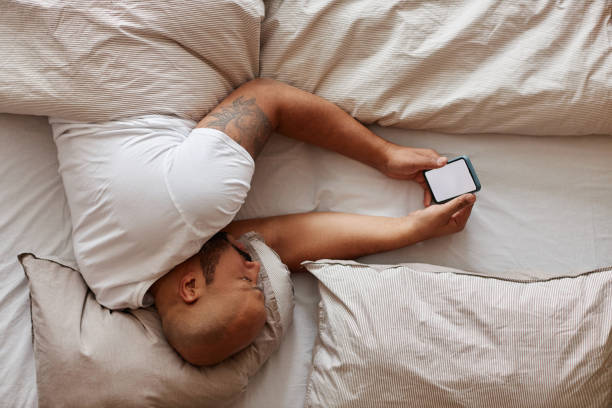 Top view of black man lying in bed and holding smartphone