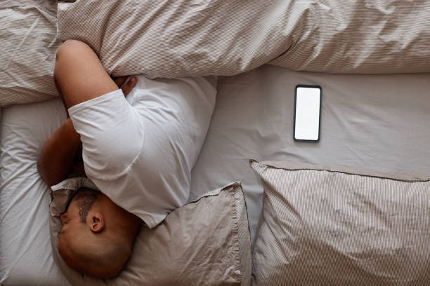 istock Top view of black man sleeping in bed with white screen smartphone mockup 1550405198