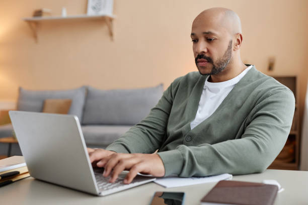istock Adult black man using laptop working from home in setting 1550405211