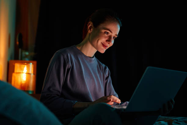 Woman using laptop in bed in dark