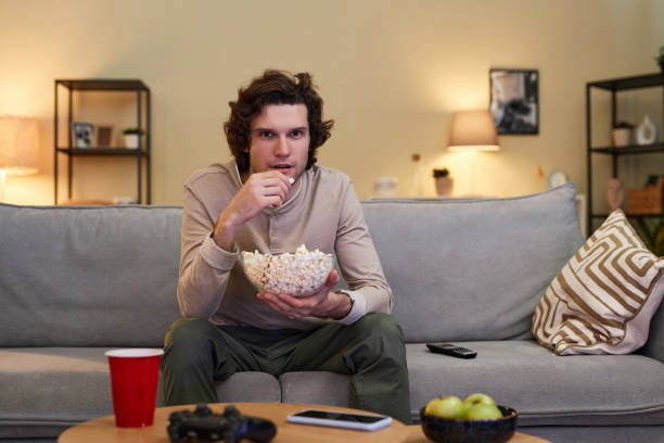 istock Man watching Tv at home and eating popcorn sitting on sofa in evening 1550415837