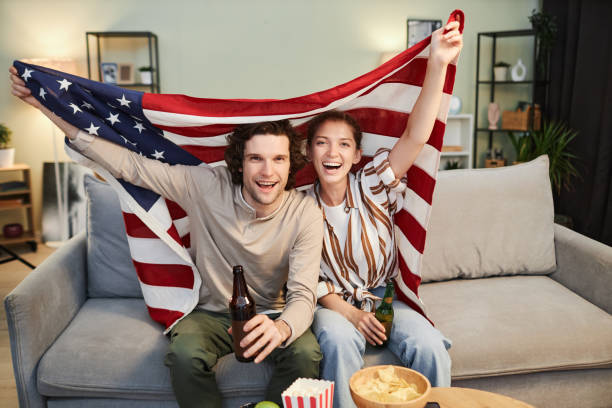 un couple brandissant le drapeau des états-unis applaudit un match sportif à domicile - lifestyles boyfriend american football cheerful photos et images de collection