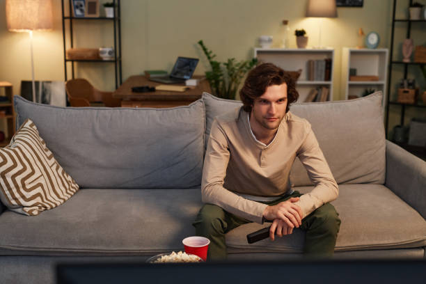 istock Smiling man watching TV at home sitting on comfortable sofa in cozy interior 1550416164