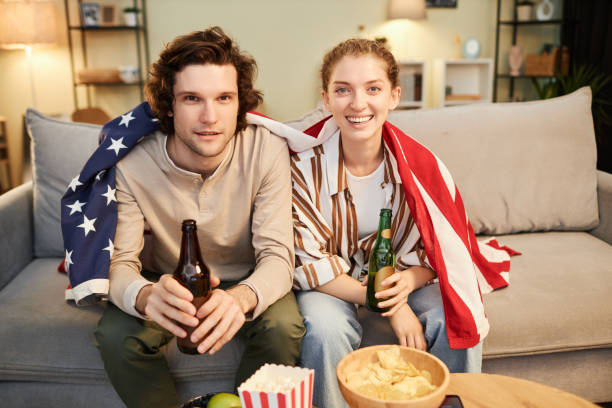 couple avec le drapeau américain regardant un match de sport à la télévision à la maison - lifestyles boyfriend american football cheerful photos et images de collection