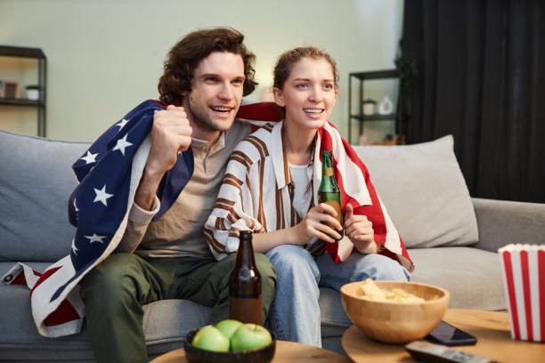 couple émotionnel avec le drapeau américain regardant un match de sport à la maison - lifestyles boyfriend american football cheerful photos et images de collection