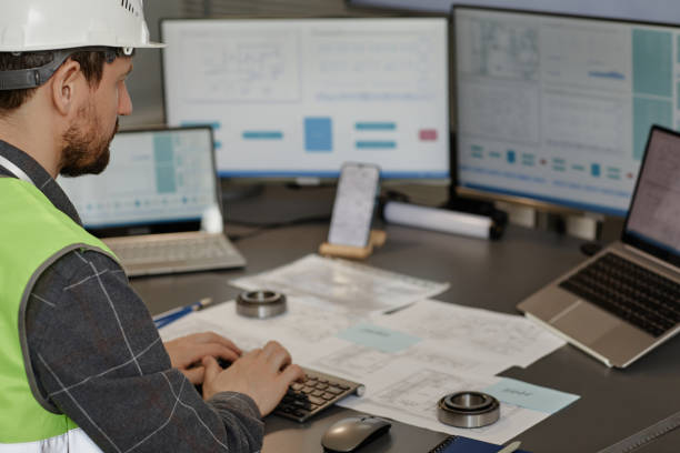 istock Male engineer wearing hardhat n office and using computer designing blueprints 1550428223