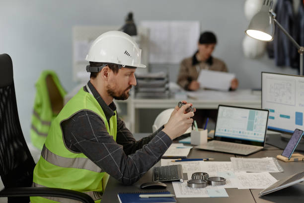 istock Male engineer holding steel machine part working on construction plans in office 1550428227
