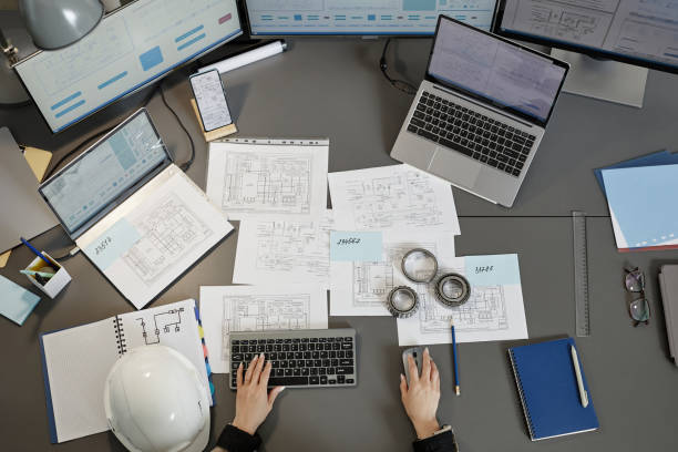 istock Top view at engineers workplace with blueprints and plans on computer desk 1550428286