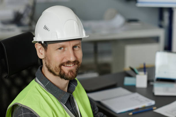 istock Bearded man wearing hardhat at workplace in office and looking at camera 1550428760