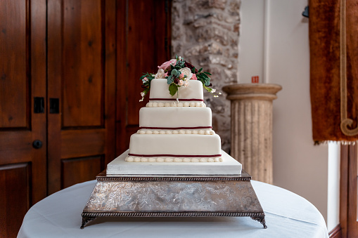 Top view of female pastry chef holding cake. White wedding cake with floral decoration on wooden stand.