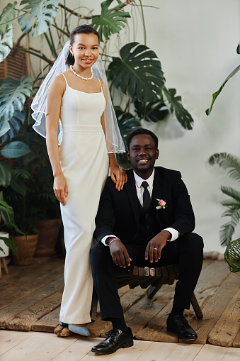 Full length wedding portrait of black young couple as bride and groom posing together in orangerie