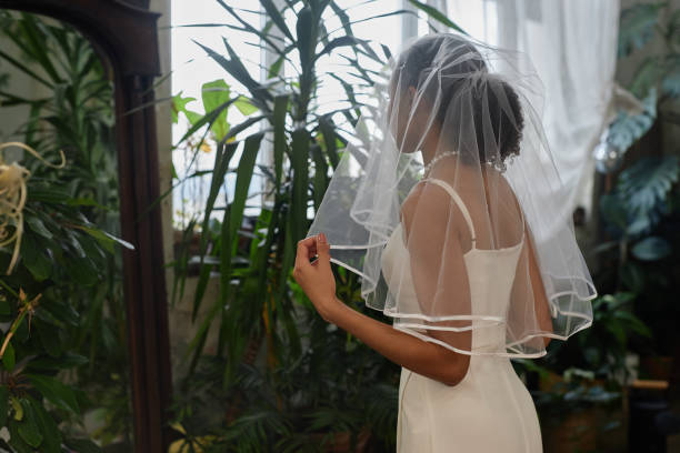 Black young woman as young bride wearing wedding gown and looking in mirror