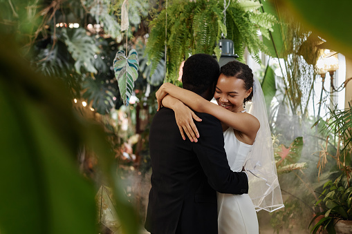Waist up portrait of young black couple getting married and dancing together in orangerie full of lush tropical plants, copy space