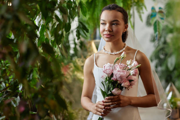 Young black bride wearing wedding gown and holding bouquet of peonies