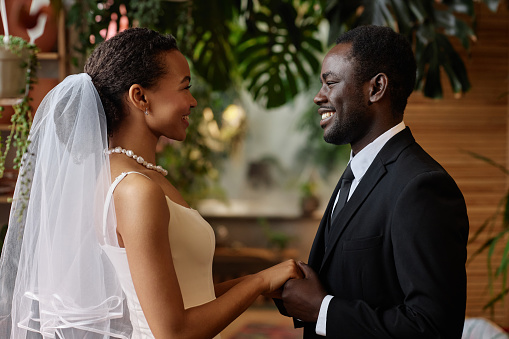 Waist up portrait of young black couple getting married and looking at each other holding hands