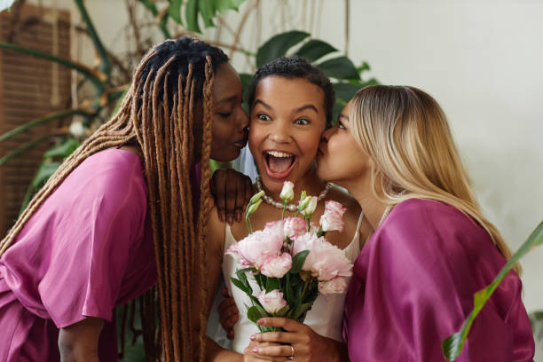 Candid two bridesmaids kissing bride on cheeks during wedding ceremony