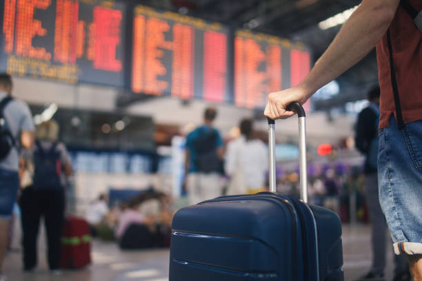 Hand of man while holding suitcase against arrival and departure board at airport Traveling by airplane. Man waiting in airport terminal. Selective focus on hand holding suitcase against arrival and departure board. Passenger is ready for travel. airport stock pictures, royalty-free photos & images