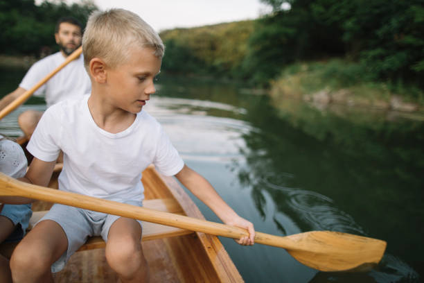 Father and son paddling a kayak on a calm, scenic river on a sunny summer day, enjoying outdoor adventure, nature, water sport, family activity