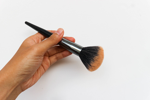 Hand holding cosmetic brush for makeup isolated on white background
