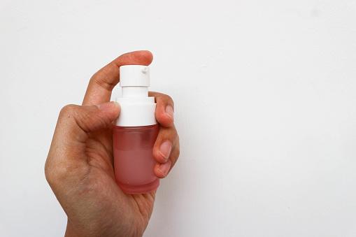 Hand holding tube of pink bottle filled with skin care cream