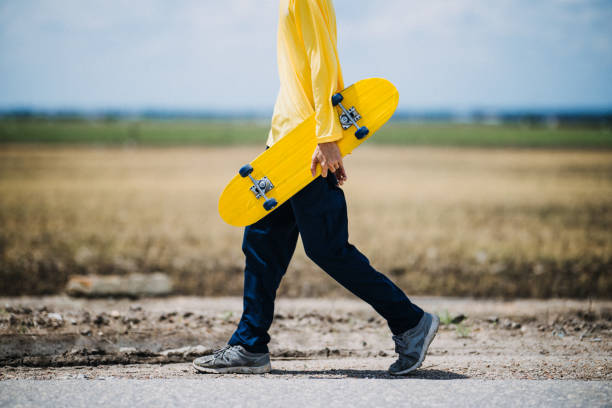 Unrecognizable man enjoying himself outdoors, riding his skateboard on an empty open road.