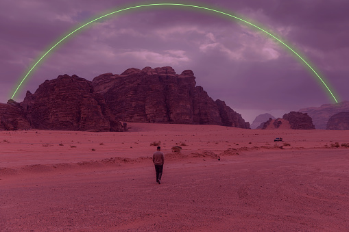 Silhouette of tourist under bright neon ellipse at dramatic martian landscape with rocks and mountains at Wadi Rum, Jordan - Metaverse, Web3 inspiration